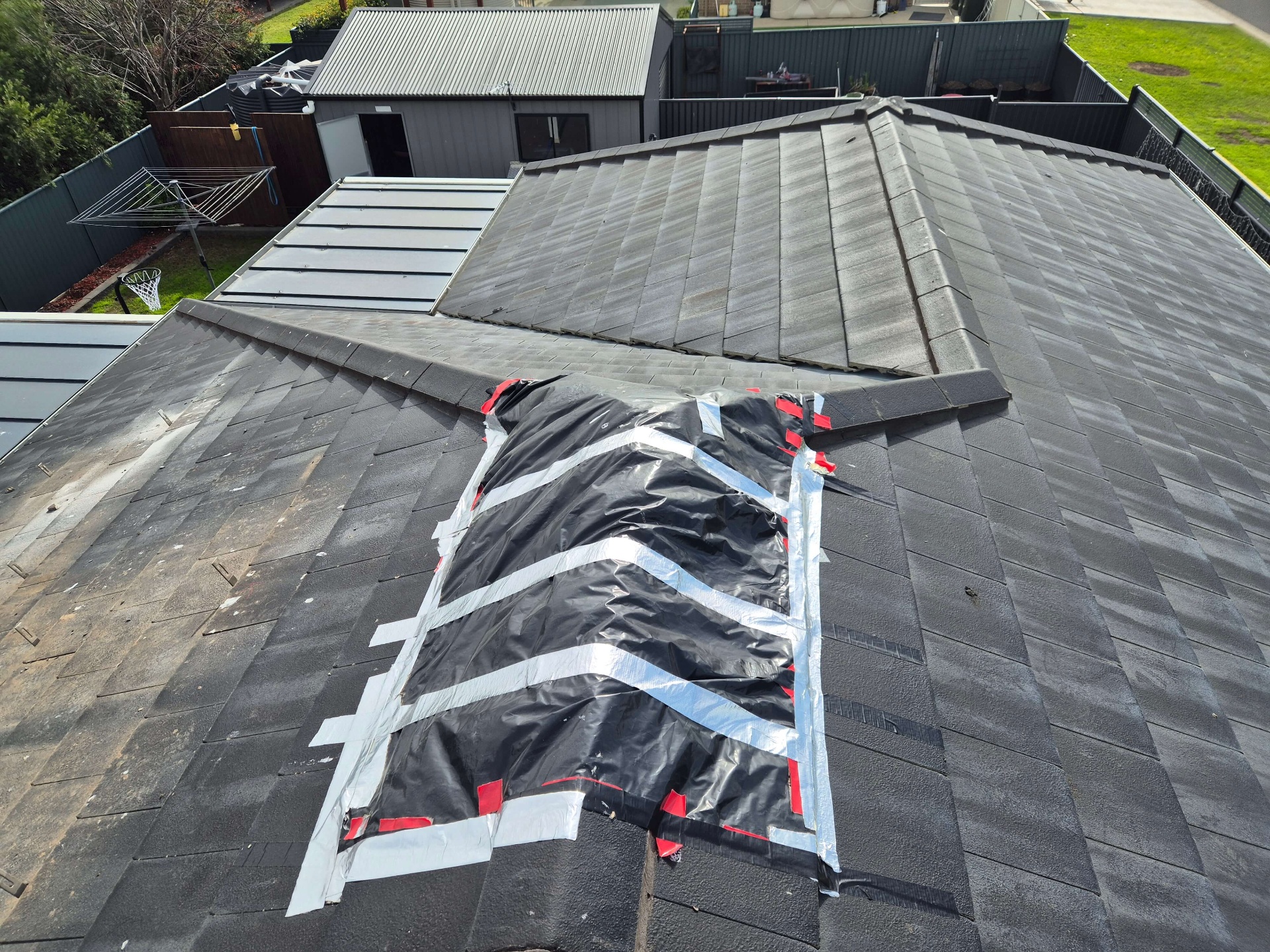 Storm-Damaged Charcoal Tile Roof With a Temporary Tarp Taped Over the Broken Section