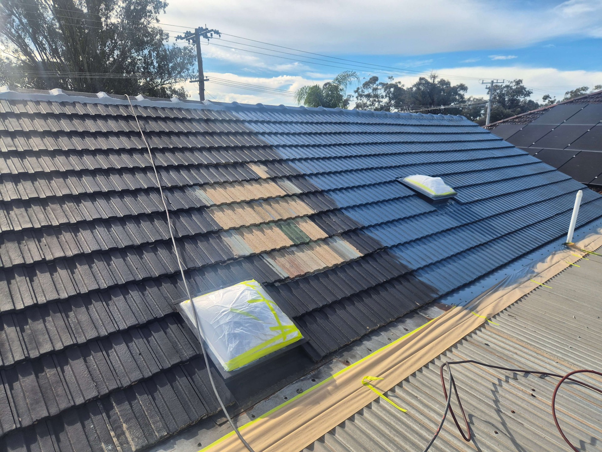 Gunnedah tile roof part-way through spray painting, with fresh blue-grey coating rolling across the tiles and skylights masked off