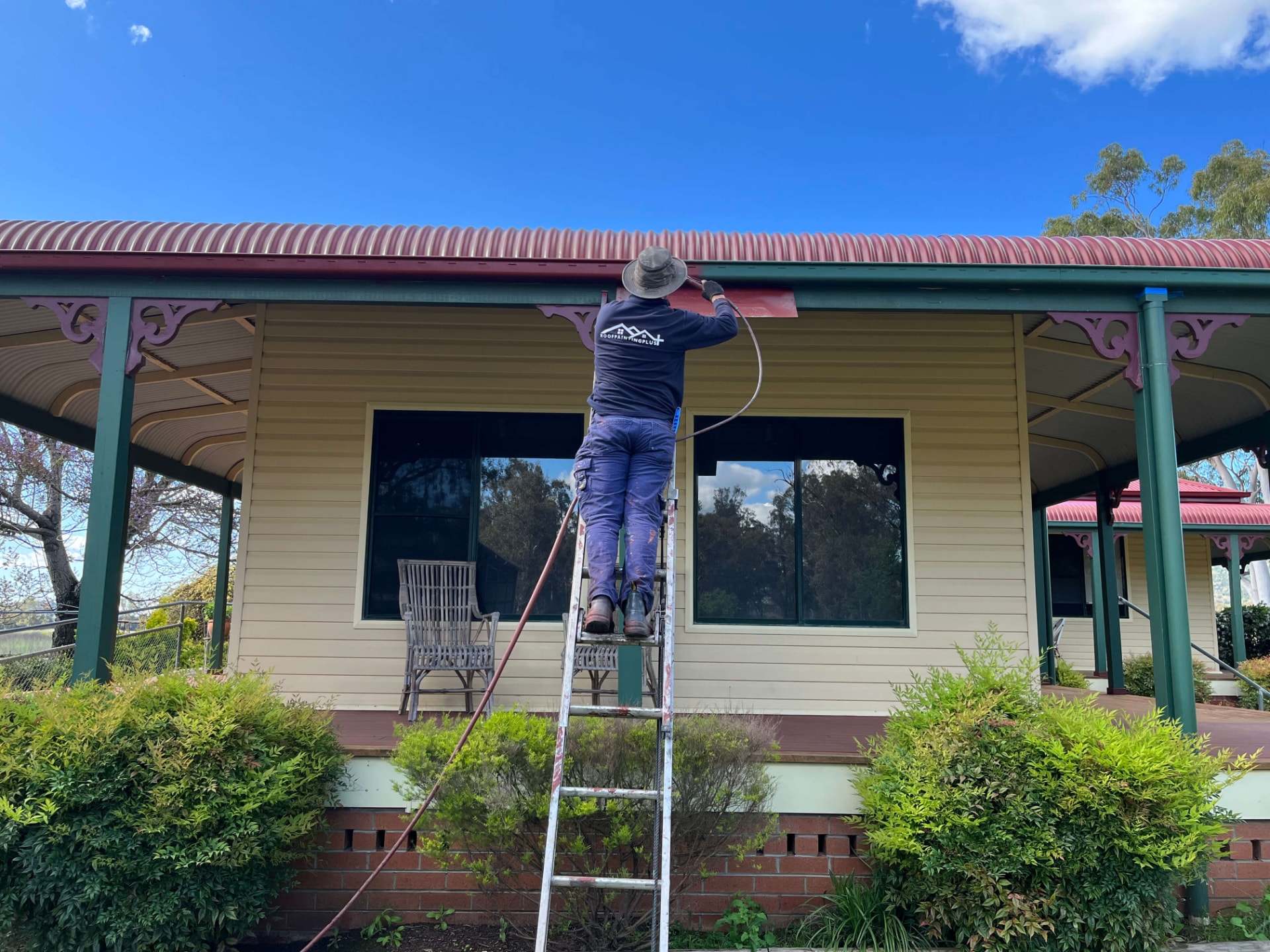 Worker Airless Spray-Painting the Fascia of a Bullnose Corrugated Metal Roof
