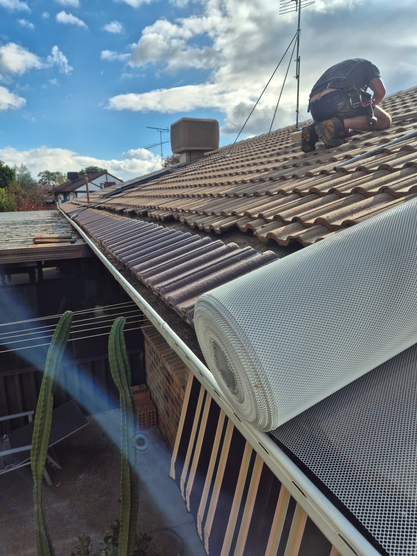 Unprotected tiled roof gutter with a roll of aluminium leaf mesh ready to install